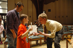David Ballintyn gives a first Communion textbook to Aaron Adrian, a second-grader at St. Mark School, during a Jan. 9 meeting at St. Mark the Evangelist Church in Indianapolis. Aaron’s father, Anthony Adrian, stands behind him.