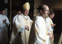 Archbishop Daniel M. Buechlein, from left, Father Christopher Wadelton and Father Sean Danda smile as they process out of SS. Peter and Paul Cathedral in Indianapolis on June 27 at the conclusion of the liturgy during which the archbishop ordained the two priests. Walking behind the archbishop is seminarian Peter Jansen, who assisted as an altar sever at the ordination Mass. (Photo by Sean Gallagher)