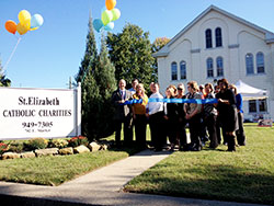 In New Albany, St. Elizabeth Catholic Charities agency director Mark Casper, third from left in the front row, cuts a ribbon on Oct. 10, 2013, marking the official opening of the agency’s new administration and social services building. Built in 1850 as the rectory for the former Holy Trinity Parish, the structure’s historic preservation and restoration was completed during the last week of June. New Albany Mayor Jeff Gahan holds the ribbon at left. (Submitted photo)