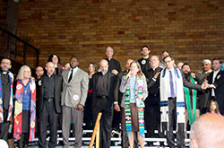 Priests and leaders of other faith congregations stand in solidarity for immigrants and refugees during an event at which Indianapolis Mayor Joe Hogsett spoke out against discriminatory practices by law enforcement against immigrants and refugees on Feb. 12 in the St. Philip Neri School gymnasium in Indianapolis. Shown in this photo are four pastors of Indianapolis parishes: Father Christopher Wadelton, pastor of St. Philip Neri Parish, third from left; Father Todd Goodson, pastor of St. Monica Parish, center; Msgr. Paul Koetter, pastor of Holy Spirit Parish, behind Father Goodson; and Father Rick Ginther, pastor of Our Lady of Lourdes Parish, second from right. (Submitted photo by IndyCAN)