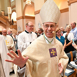 Archbishop Charles C. Thompson smiles and waves to members of the congregation as he processes on July 28 into SS. Peter and Paul Cathedral in Indianapolis at the start of the Mass in which he was installed as the seventh archbishop of Indianapolis. Behind him is Father Patrick Beidelman, rector of the cathedral, who served as a master of ceremonies for the liturgy. (Photo by Rob Banayote)