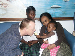 In a lighthearted moment, Holy Family Shelter director Bill Bickel, left, pretends to take a cracker from Tonika Mitchum, the 1-year-old daughter of Jolanda Mitchum, second from left. Tonika and Jolanda reside at the shelter. Tonika is being held by Nigisty Christos, Bickel’s administrative assistant.
