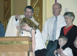 Father Christopher Craig, pastor of St. Mary of the Immaculate Conception Parish in Aurora, baptizes Molly Schmahl during the parish’s Easter Vigil on April 7. Molly’s parents, Kurt and April Schmahl, and her younger brother, Noah, look on. Kurt, Noah, and two of Molly’s older sisters were also received into the Church during the liturgy. (Submitted photo) 