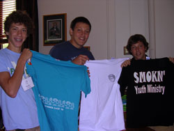 Members of the SMOKN’ Youth Ministry of St. Mary-of-the-Knobs Parish in Floyds Knobs and St. Mary Parish in Navilleton display a few of the T-shirts they will trade with “One Bread, One Cup” participants from other communities. From left are Matthew Hamilton, Paul Crockett and Kevin Crockett, all members of St. Mary-of-the-Knobs Parish. Their group’s slogan is “We’re fired up for Jesus.” (Photo by Patricia Happel Cornwell) 