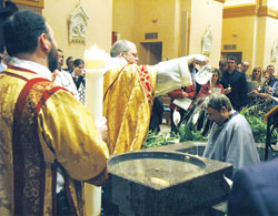 Benedictine Father Julian Peters, administrator pro-tem of SS. Peter and Paul Cathedral Parish in Indianapolis, baptizes Scott Warpool during Cathedral Parish’s Easter Vigil on March 22. Transitional Deacon Aaron Jenkins, holding the parish’s Easter candle, stands at left. (Photo by Sean Gallagher)
