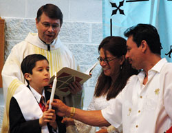 Tyler James, a Special Religious Education participant at St. Simon the Apostle Parish in Indianapolis, holds his baptismal candle as Father Daniel Staublin, pastor of St. Malachy Parish in Brownsburg, watches with Tyler&rsquo;s parents, Dr. Nettie Viera and Richard James, during the archdiocesan SPRED Mass on April&nbsp;27 at St. Mark the Evangelist Church in Indianapolis. (Photo by Mary Ann Wyand)