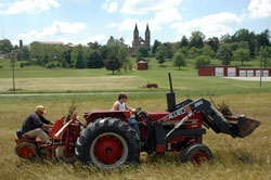 Farmers work in a field in Spencer County. Saint Meinrad Archabbey’s Church of Our Lady of Einseideln is visible in the distance. Rural parishes like nearby St. Meinrad Parish in St. Meinrad and others throughout the Archdiocese of Indianapolis offer a unique connection of faith and family. (Photo by John Farless)