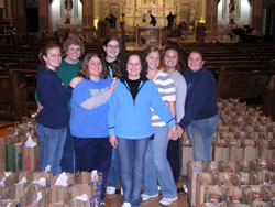 Members of the extended Hammans family help to keep alive the Holy Cross Parish tradition of feeding the needy at Thanksgiving and Christmas. Andrea Hammans, left, Mary Hammans Qualls, Ann Tobin Pliler, Candice Qualls, Lori Hammans Tobin, Amy Tobin Kinnaman, Cecelia Hammans and Kelly Qualls stand with bags of food. (Photo by John Shaughnessy) 
