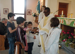 Father Dominic Chukwudi receives offertory gifts from Amanda Tovey, left, C. J. Murrary, Virginia Graf and Jacob Bray during a Nov. 9 Mass at Holy Rosary Church in Seelyville. Assisting Father Chukwudi are altar servers Sara Baugh, left, and Molly Tovey. A priest of the Diocese of Issele-Uku, Nigeria, Father Chukwudi has ministered in the archdiocese since 2006 and is currently the administrator of Annunciation Parish in Brazil and Holy Rosary Parish in Seelyville. (Photo by Sean Gallagher) 