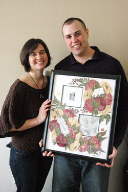 Stephanie and Christopher Fenton of St. Jude Parish in Indianapolis hold a framed picture containing their wedding invitation, flowers and her A Promise to Keep pin, which she carried in her bridal bouquet on their wedding day. The Fentons found that the communication and relationship skills they learned as chastity peer mentors during their senior year in high school in 2000 helped them stay close as a couple during his deployment to Iraq in 2008. (Photo by Mary Ann Wyand) 