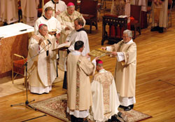 Archbishop Charles J. Chaput of Denver prays a prayer of consecration over a kneeling Bishop-designate Paul D. Etienne during a Dec. 9 episcopal ordination and installation liturgy at the Cheyenne Civic Center in Cheyenne Wyo. Deacons Tim Martinson, from left, and Doug Vlchek, both of the Cheyenne Diocese, hold a Book of the Gospels over Bishop-designate Etienne’s head, which, among other things, symbolizes the yoke that Christ invited his followers to take upon themselves. (Photo by Sean Gallagher)