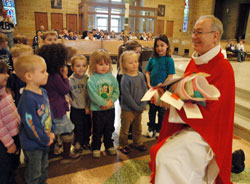 Father Robert Gilday, right, receives a spiritual bouquet from Canaan Miller, from left, Gabrielle Herner, Gavin Turner, Lily Russell, Mira Jackson and Shelby Robinett, all preschool students at Little Flower School in Indianapolis, during a Feb. 5 Mass at the parish church. Father Gilday is the pastor of St. Therese of the Infant Jesus (Little Flower) Parish. (Photo by Sean Gallagher)