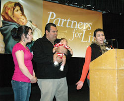 Mariana Ruiz, right, speaks as a translator for her uncle and Gabriel Project volunteer, Luis Aguayo, second from left during a March 23 Gabriel Project fundraising banquet in Indianapolis. Aguayo is holding Emil Lopez, the son of Maria Lopez, left. Emil was saved from abortion through the assistance of Aguayo and other Gabriel Project volunteers. (Photo by Sean Gallagher)