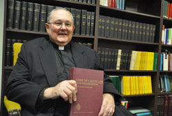 Msgr. Frederick Easton, now adjunct vicar judicial, holds a copy of the Code of Canon Law while sitting in a conference room of the archdiocese’s Metropolitan Tribunal in the Archbishop Edward T. O’Meara Catholic Center in Indianapolis on Oct. 6. Msgr. Easton led the tribunal as its vicar judicial for 31 years before retiring in July. (Photo by Sean Gallagher)