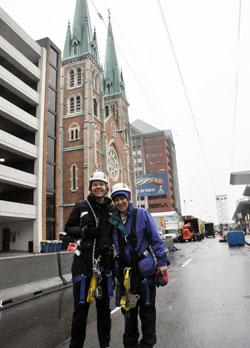 Benedictine Sisters Jennifer Mechtild Horner, left, and Sheila Fitzpatrick pose under the 800-foot zip line they rode on Jan. 26 that was built over Capitol Avenue in Indianapolis in the middle of the Super Bowl Village next to St. John the Evangelist Church. Both sisters are members of Our Lady of Grace Monastery in Beech Grove, which is hosting the workers that constructed and are operating the zip line. (Photo by Sean Gallagher)