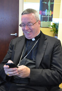 Bishop Christopher J. Coyne, apostolic administrator, smiles as he types a Twitter message on his cell phone during a break between speakers at a National Catholic Youth Conference press conference for local media on Oct. 19, 2011, at the Indiana Convention Center in Indianapolis. (Photo by Mary Ann Garber)