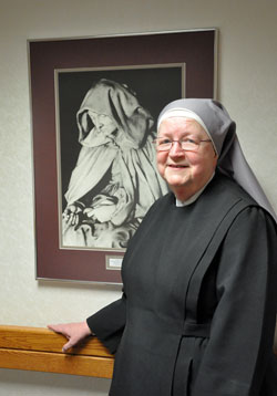 Mother Mary Vincent Mannion, superior of the Little Sisters of the Poor at the St. Augustine Home for the Aged in Indianapolis, poses for a recent photo beside a portrait of St. Jeanne Jugan, the order's foundress, at the home for the elderly poor. Residents enjoy the opportunity to participate in Mass each day at the home's chapel. (Photo by Mary Ann Garber)