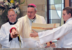 Bishop Christopher J. Coyne, apostolic administrator, pours chrism oil on the new altar at St. Mary-of-the-Knobs Church as Father Patrick Beidelman, left, master of ceremonies and director of liturgy for the archdiocesan Office of Worship, and altar server Trenton Law of Georgetown, right, assist him. (Photo by Mary Ann Garber)