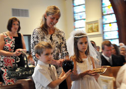 Trevor Langley, front left, and Lily Thomas, right, bring up the offertory gifts during the first Communion Mass on April 22 at St. Ann Church in Terre Haute. Catechist Lisa Ferguson, back left, and religious education coordinator Marti Goodwin help the children. (Photo by Mary Ann Garber)
