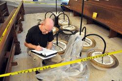Eric Atkins, director of management services for the archdiocese, inspects the light bulb and chandelier that caused a fire on June 2 at St. Christopher Church in Indianapolis. No estimate of the fire, smoke and water damage is available yet. Restoration work began shortly after firefighters extinguished the blaze. (Photo by Mary Ann Garber)