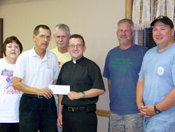 Father Steven Schaftlein, second from left, wanted to share a $100,000 donation for tornado relief that he had received as the pastor of St. Francis Xavier Parish in Henryville with the people of Holton, another community devastated by the March 2 storms. So he made the check presentation during a surprise visit at a meeting of the Holton Long Term Recovery Group. He is pictured with, from left, Cynthia Melton, case manager of the group; Norm Knudson, the group’s secretary/treasurer; Father Shaun Whittington, pastor of St. John the Baptist Parish in Osgood; Darin Kroger, the group’s construction manager; and Philip Diewert, the group’s volunteer manager. (Submitted photo)