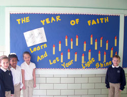 Amelia Harrigan, left, Meredith Attai, Hailey Kocher and Gavin Farris, all second-grade students at St. Roch School in Indianapolis, pose on Jan. 15 in front of a bulletin board at their school dedicated to the Year of Faith. Each student wrote a way to evangelize on the bulletin board candles. Answers included, “I will give food to the poor,” and “I will proclaim the word to others.” (Submitted photo)