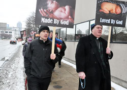 Father John Hollowell, left, and Archbishop Joseph W. Tobin pray the rosary on Jan. 25 while leading more than 400 pro-life supporters in a march up and down several blocks of Meridian Street in Indianapolis. The march and Mass at SS. Peter and Paul Cathedral that preceded it took place to commemorate the 40th anniversary of the Supreme Court decisions that legalized abortion in the United States in 1973. (Photo by Sean Gallagher)