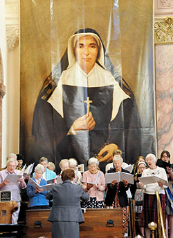 Members of the Sisters of Providence choir, joined by the Saint Mary-of-the-Woods College Chorale, sing during the Mass celebrating the feast of St. Theodora at the Church of the Immaculate Conception in St. Mary-of-the-Woods on Oct. 3. The wooden box in front of the choir director contains the remains of St. Theodora, and the hanging banner was the one displayed in St. Peter’s Square at the Vatican when the founder of the Sisters of Providence was beatified in 1998. (Photo by Natalie Hoefer)