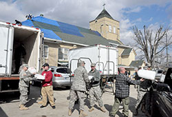 Members of the Indiana National Guard and other rescue workers load ice on March 3, 2012, into a refrigerated truck parked next to St. Francis Xavier Church in Henryville, Ind., while workers attach a tarp to the church’s damaged roof that resulted from a tornado the previous day. Archdiocesan Catholics were generous in helping those affected by the storm, raising nearly $250,000 in a special collection. (File photo by Sean Gallagher)