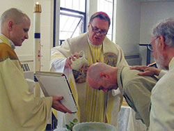 Archbishop Joseph W. Tobin baptizes Frank Wederzak during an April 22 Mass at the Putnamville Correctional Facility in Putnamville. Wederzak is an inmate at the prison. He and five other inmates were baptized and received into the full communion of the Church. Father John Hollowell, left, chaplain at the facility and pastor of Annunciation Parish in Brazil and St. Paul the Apostle Parish in Greencastle, assists in the rite of baptism. Bernie Batto, right, a member of St. Paul Parish, serves as Wederzak’s sponsor. (Submitted photo)