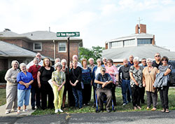 Members of the St. Lawrence School Class of 1961 in Indianapolis gather around a street sign on the parish campus on Sept. 18. Through a school fundraiser auction, class member Betsy Kinne Smith, standing in front of the sign in yellow, won the right to name the sign. On behalf of the class of 1961, she named it for their classmate Lt. Gen. Timothy Maude, the highest ranking officer killed in the Sept. 11, 2001 terrorist attacks. (Photo by Natalie Hoefer)