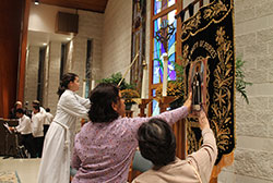 Marilou Eria, center, a native of the Philippines and now a member of Our Lady of the Greenwood Parish in Greenwood, shares a quiet moment of devotion before a banner depicting St. Martin de Porres on Nov. 3. A Mass honoring the saint was celebrated that evening at St. Mark the Evangelist Church in Indianapolis. (Submitted photo by Victoria Arthur)