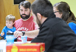 Ryan Raelson holds his son Sawyer while playing Apples to Apples Bible Edition with his wife Sarah (partially obscured) and seminarian Michael Bower during a family game night at Holy Name Parish in New Albany on March 2. (Photo by Natalie Hoefer)