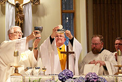 Msgr. Frederick Easton, center, elevates the Eucharist during a May 1 Mass at St. Charles Borromeo Church in Bloomington that celebrated the 50th anniversary of his priestly ordination. Assisting at the Mass are Deacon Marc Kellams, left, and master of ceremonies Father Joseph Newton, second from right. Archbishop Joseph W. Tobin is seen at right. (Submitted photo)