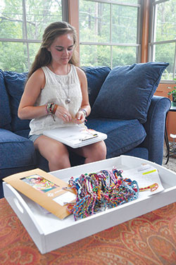 Scores of friendship bracelets in the foreground are ready to be shipped to the international nonprofit Unbound while their creator, Cathedral High School senior Rachel Kent of Indianapolis, makes another to add to the stack. For each bracelet she sells, Rachel makes one for Unbound to give to an impoverished child in a foreign country, and gives all proceeds to the layCatholic founded organization. (Photo by Natalie Hoefer) 