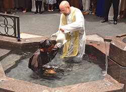 Father Todd Goodson, pastor of St. Monica Parish in Indianapolis, baptizes Gilaniche Codjo Senou, 28, during the Easter Vigil on April 15. (Submitted photo by Katherine Gatons)	