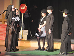 Students of St. Joseph School in Shelbyville act on March 19 in a scene from the St. Joe Show at the Strand Theater in Shelbyville, a play about the founding of St. Joseph Parish written by its administrator, Father Michael Keucher. The students playing Franciscan sisters are Macey Robbins, left, Leah Smothers and Molly Johnson. Taylor Abell and Tyler Gwinnup, center, act as the mayor of Shelbyville and his wife, and Charlie Fischer, at right, plays Father Francis Rudolf, founder of St. Joseph School and the parish’s first resident pastor. (Photo by Sean Gallagher)