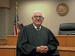 Wearing the robes of a judge, Deacon Marc Kellams stands on Oct. 15 in the courtroom of the Monroe County Circuit Court in Bloomington where he serves as judge. After his service of nearly 40 years as a judge in Monroe County comes to an end later this year, Deacon Kellams will begin ministry as the coordinator of corrections ministry for the archdiocese. He was ordained a permanent deacon for the archdiocese in 2008. (Photo by Katie Rutter)