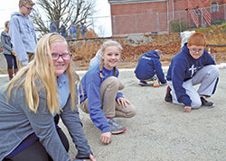 Mary Schmidl, left, Lilah Butz and Henry Schneider, all sixth-graders at St. Nicholas School in Ripley County, place blessed medals of saints in gravel on Nov. 5, 2018, where a foundation was later laid for a new education center at the Batesville Deanery faith community. (Submitted photo)