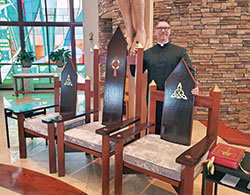 Father Sean Danda, pastor of St. Malachy Parish in Brownsburg, stands proudly with the three sanctuary chairs custom-designed and built by parishioners in time for the parish’s feast day Mass in November 2018 during the faith community’s sesquicentennial year. The artisans volunteered at least 1,600 hours on the project. (Submitted photo)