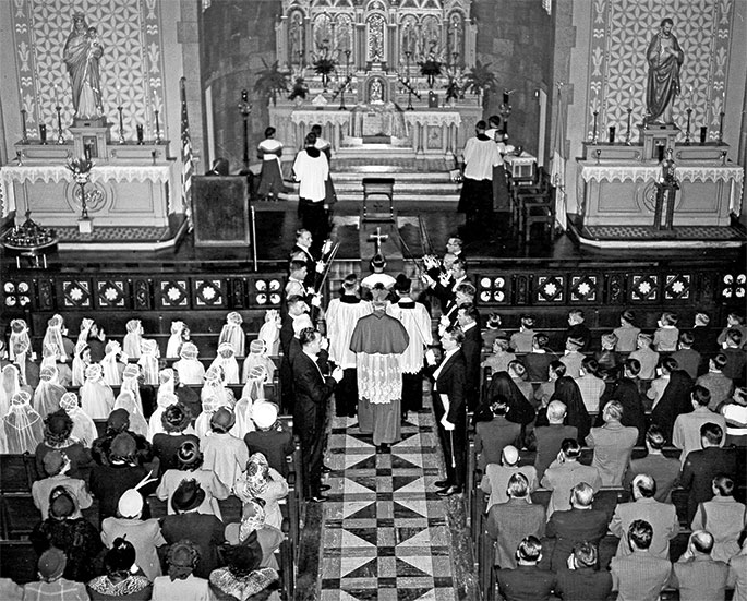 This photo depicts a confirmation liturgy at St. Lawrence Church in Lawrenceburg. There is no date included with the photo, but a second photo in the archives from the same day indicates that the pastor was Father Herman Kasper, who led the parish from 1949-1962. Archbishop Paul C. Schulte is seen processing into church to administer the sacrament. 