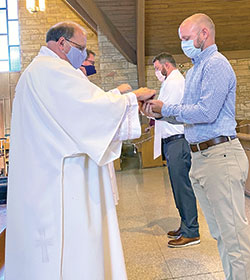 Drew Haynes, right, receives the Eucharist from Deacon Jeffrey Powell, left, for the first time at Our Lady of Perpetual Help Church in New Albany on June 10 during a special Mass to welcome candidates and catechumens into full communion with the Church. (Submitted photo)