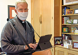Retired Msgr. Paul Koetter types into a tablet on Oct. 29 in his office at Holy Spirit Parish in Indianapolis, where he previously served as pastor. Amyotrophic lateral sclerosis, commonly known as Lou Gehrig’s disease, has taken away his ability to speak. He types what he wants to say, and software on his tablet vocalizes his words in what sounds like his voice. (Photo by Sean Gallagher)