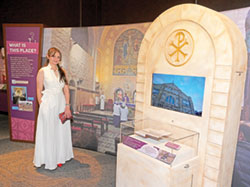 Jude Anton Twal poses in front of the area of the “Sacred Places” exhibit at The Children’s Museum of Indianapolis that features her, her Christian faith and her Catholic parish church, The Beheading of St. John the Baptist Catholic Church in Madaba, Jordan. (Photo courtesy of The Children’s Museum of Indianapolis)
