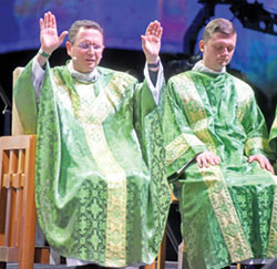 Bishop Andrew H. Cozzens of Crookston, Minn., raises his hands in personal prayer after Communion during the Nov. 18 closing Mass of the National Catholic Youth Conference at Lucas Oil Stadium in Indianapolis. Assisting at the Mass at right is archdiocesan transitional Deacon Samuel Rosko. (Photo by Sean Gallagher)