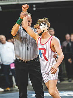 A referee raises the arm of Peyton Schoettle, signifying that the sophomore from Roncalli High School in Indianapolis has won the 106-pound match in Indiana’s state wrestling championship meet on Feb. 17. (Photo courtesy of Pure Impact Studios, LLC)