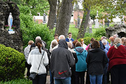 St. Michael the Archangel associate pastor Father Benjamin Ross (center) leads participants praying the Rosary during the 'Lourdes Virtual Pilgrimage' at the Schererville church's Lourdes grotto on May 14. The event, coordinated by the North American Lourdes Volunteers, included a presentation and Eucharistic Adoration. (Anthony D. Alonzo photo)