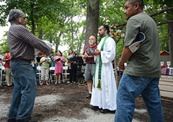 Migrant worker Pancho Gallardo brings a basket with Offertory gifts to Father Jaime Perea, as altar server Roy Wallace (center) and migrant worker Juan Alvarez look on during the Mass for migrant workers at County Line Orchard in Hobart on July 17. (Anthony D. Alonzo photo)