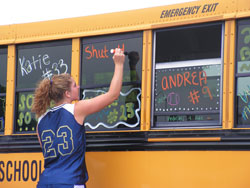 Junior catcher Elaine Rorick puts finishing touches on the team bus windows before the Bishop Dwenger Lady Saints board the bus and head for their first-ever state softball appearance.
