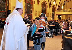 Archbishop Joseph W. Tobin receives offertory gifts from Pablo Mores, left, Maria Mores and their granddaughter, Andrea Nicole Corona, during a Dec. 12, 2012, Mass for the feast of Our Lady of Guadalupe at St. Anthony Church in Indianapolis. (File photo by Sean Gallagher) 